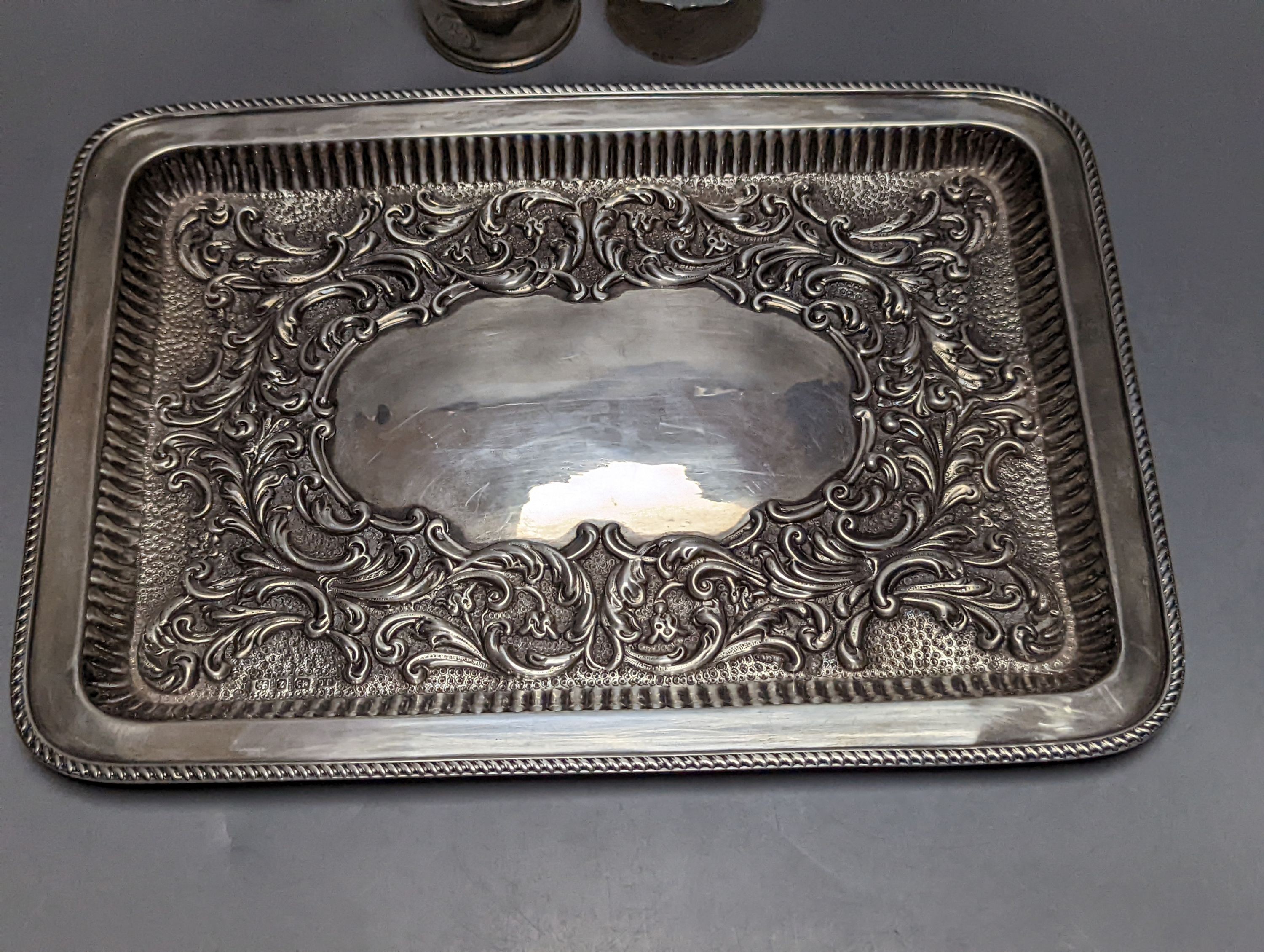 A late Victorian repousse silver rectangular dressing table tray, Joseph Gloster, Birmingham, 1899, 27.2cm, 10oz, two silver napkin rings, a silver cream jug and a silver mounted glass scent bottle.